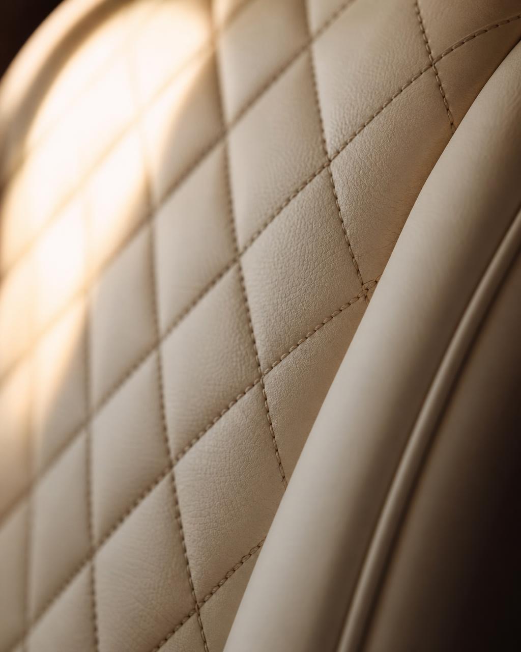 Close detail of cream diamond-quilted VVIP helicopter cabin leather, lit from one side