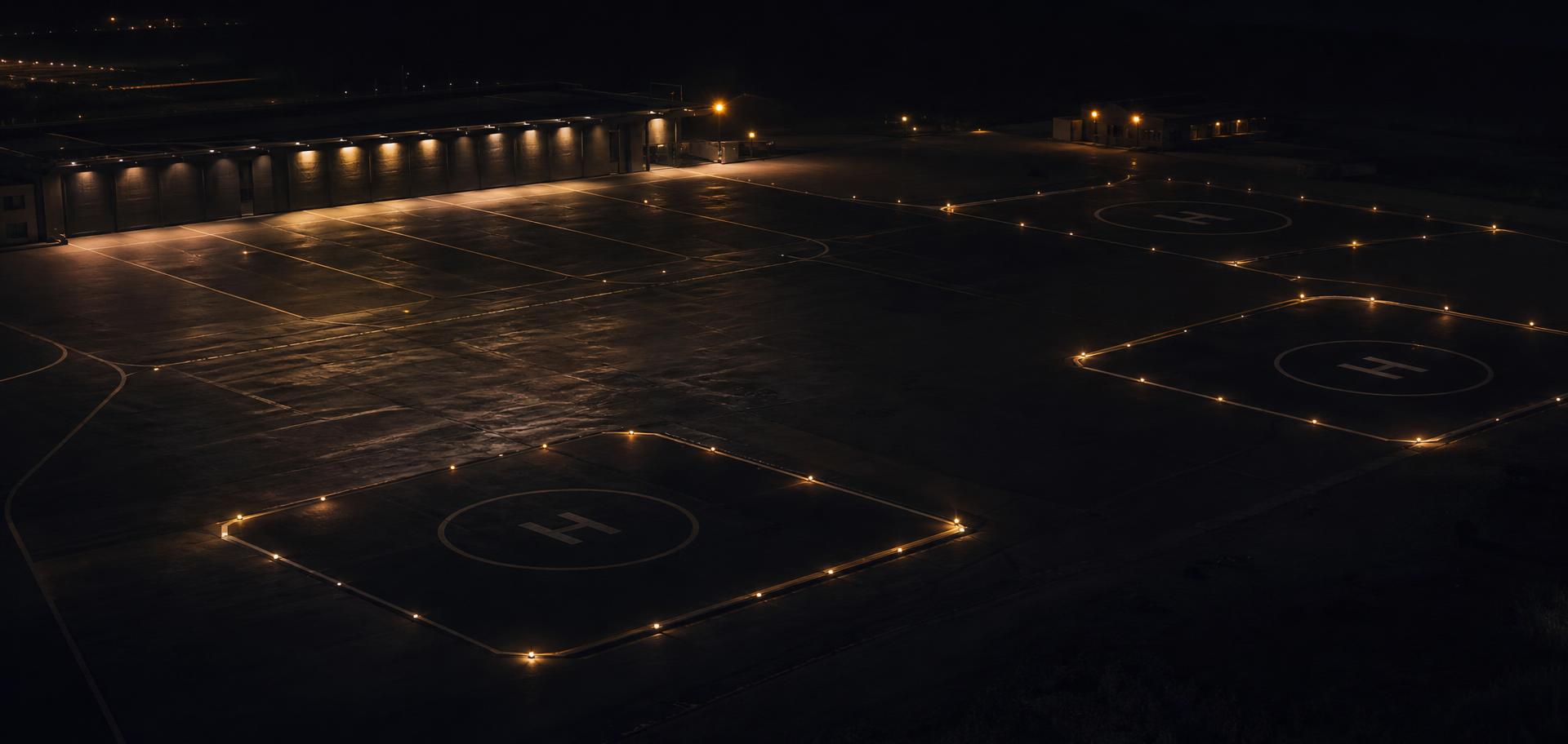 Private aviation apron at night, helipad edge lights glowing on dark tarmac